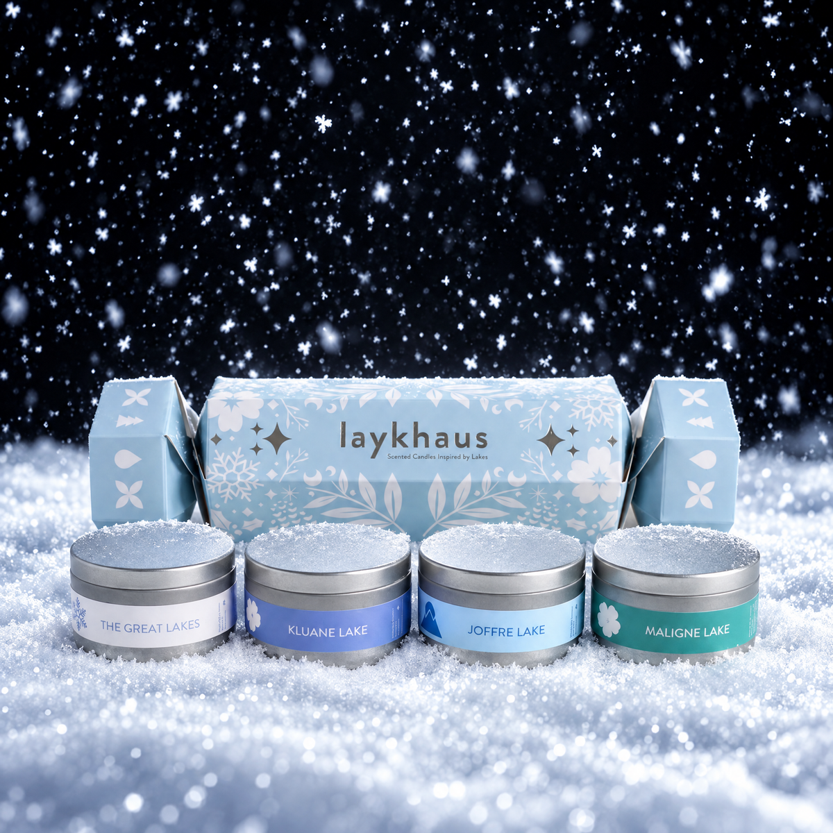 A Laykhaus winter-themed gift set featuring four small silver tins with blue labels in front of a matching blue decorative box, all styled in a snowy scene with a dark starry sky background.